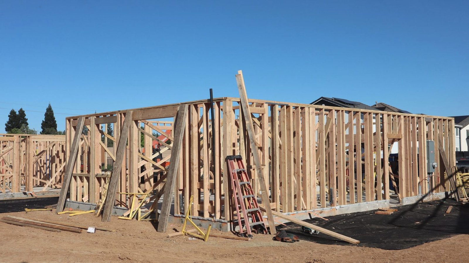 Long exterior wood-framed wall of a building under construction in bright sun.