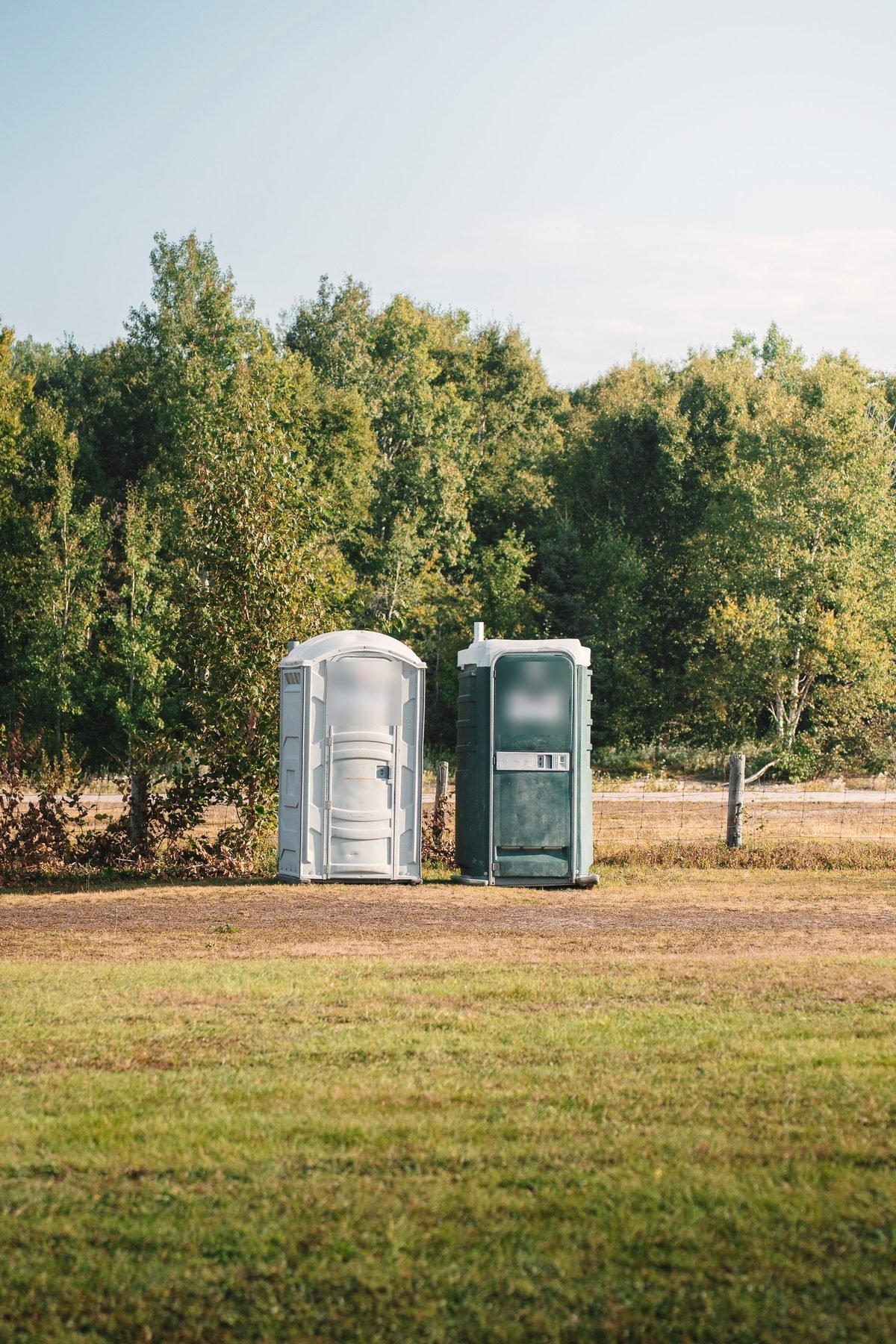 Portable restroom unit standing at the edge of a mown field.